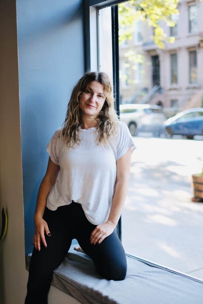 Relaxed woman practicing yoga at Bedstuy Yoga studio in Brooklyn, standing by a large window.