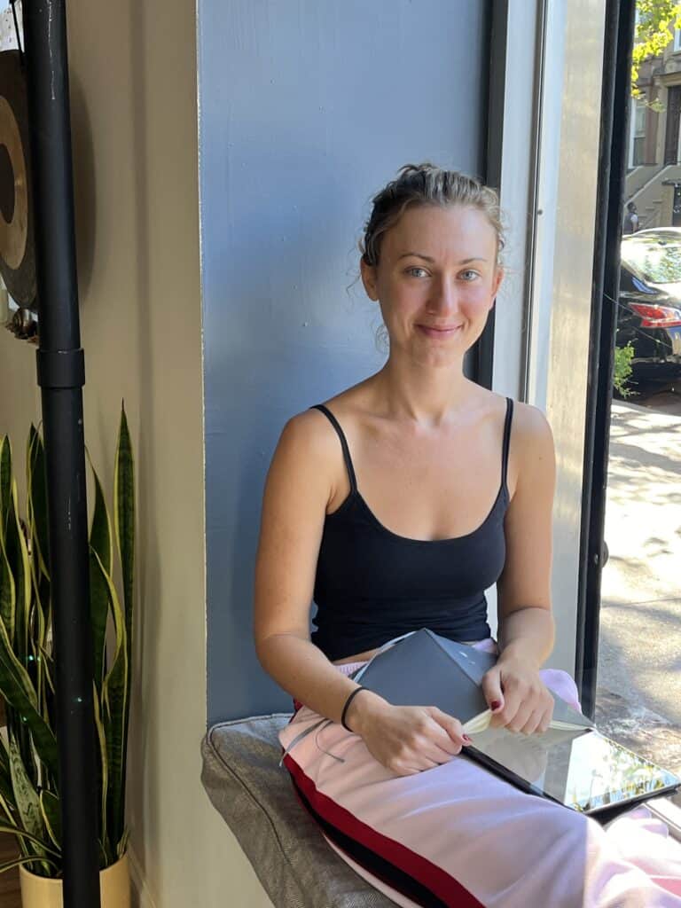 Relaxed woman sitting by a large window at Bedstuy Yoga studio, Brooklyn, practicing yoga and mindfulness.