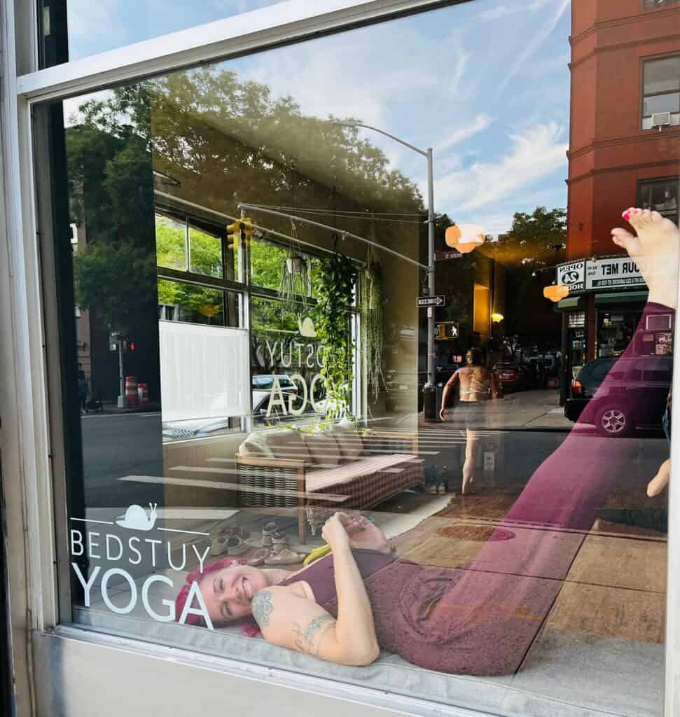 Relaxing woman practicing yoga inside Bedstuy Yoga studio on a sunny day.