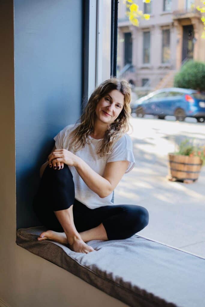 Comfortable woman practicing yoga in cozy studio window seat with city view.