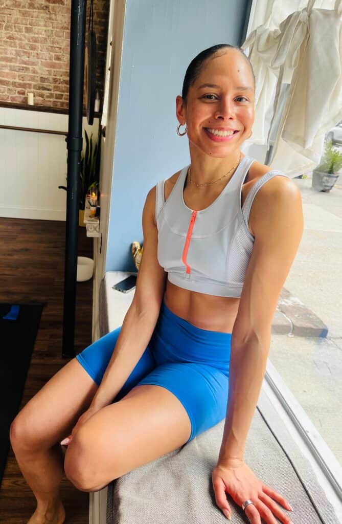Yoga instructor smiling in studio, promoting wellness and fitness.