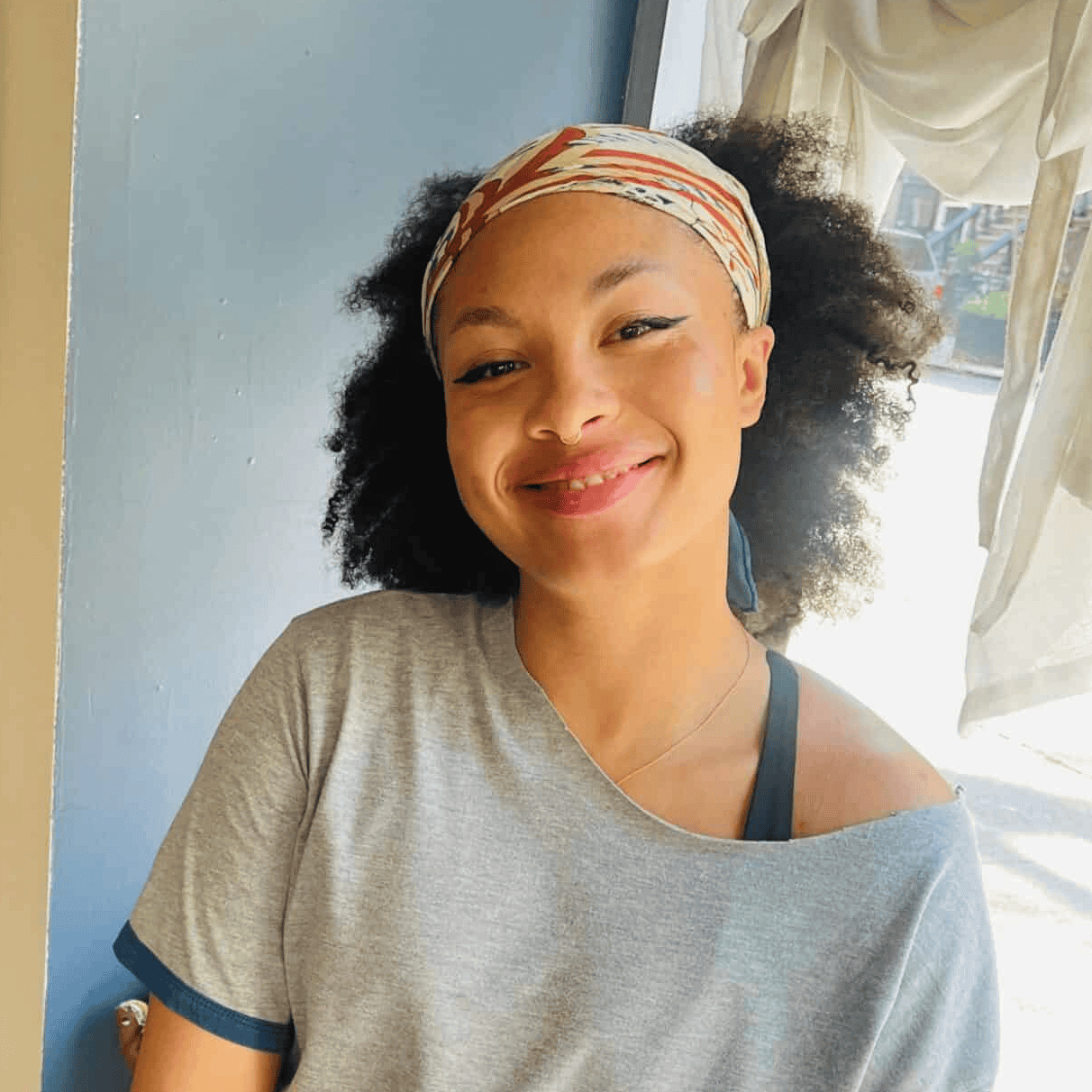 Smiling woman with curly hair and colorful headband in a yoga studio.